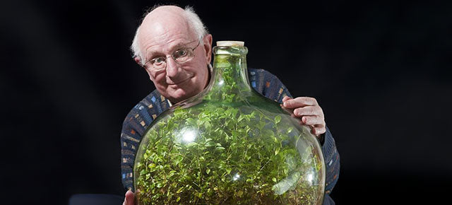 David Latimer sorridente mentre abbraccia con orgoglio la sua grande damigiana in vetro contenente il famoso giardino in bottiglia, un rigoglioso ecosistema autosufficiente chiuso dal 1972.